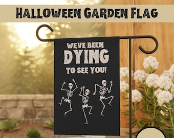 May include: A black Halloween garden flag with three skeletons dancing and the text "We've Been Dying To See You!" The flag is 12 inches by 18 inches.