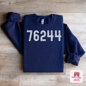 May include: Navy blue sweatshirt with the number 76244 printed in white on the front. The sweatshirt is folded in half and laid on a wooden surface.