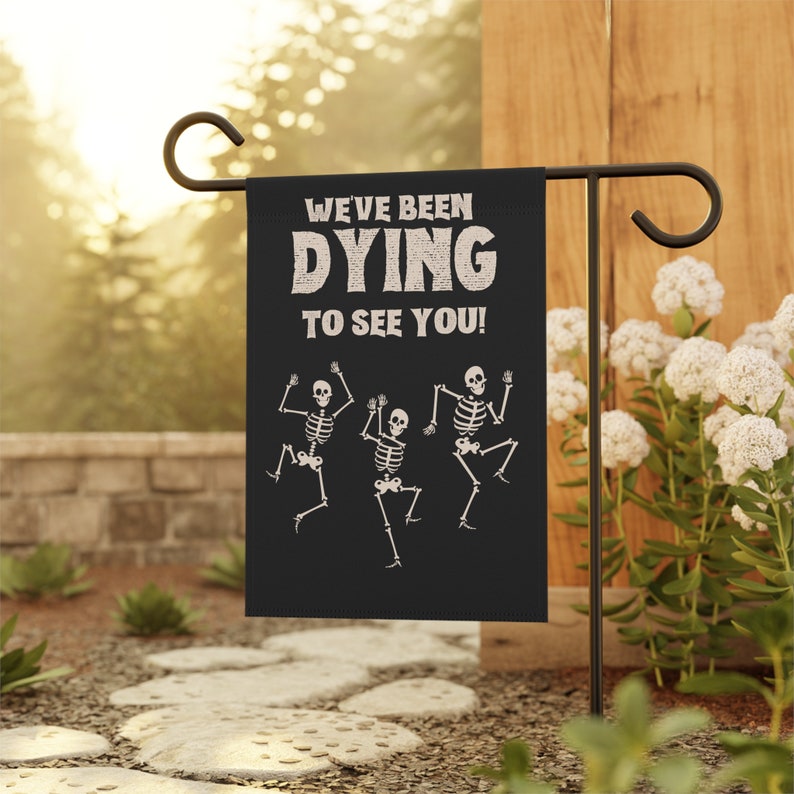 May include: A black Halloween garden flag with three white skeletons dancing and the text "We've been DYING to see you!"