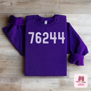 May include: Purple sweatshirt with the number 76244 printed in white on the front.