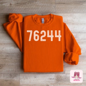 May include: Orange sweatshirt with the number 76244 printed in white on the front.