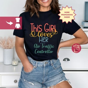 May include: A black t-shirt with the text "This Girl Loves Her Air Traffic Controller" in colorful letters. The text is in a fun, whimsical font.