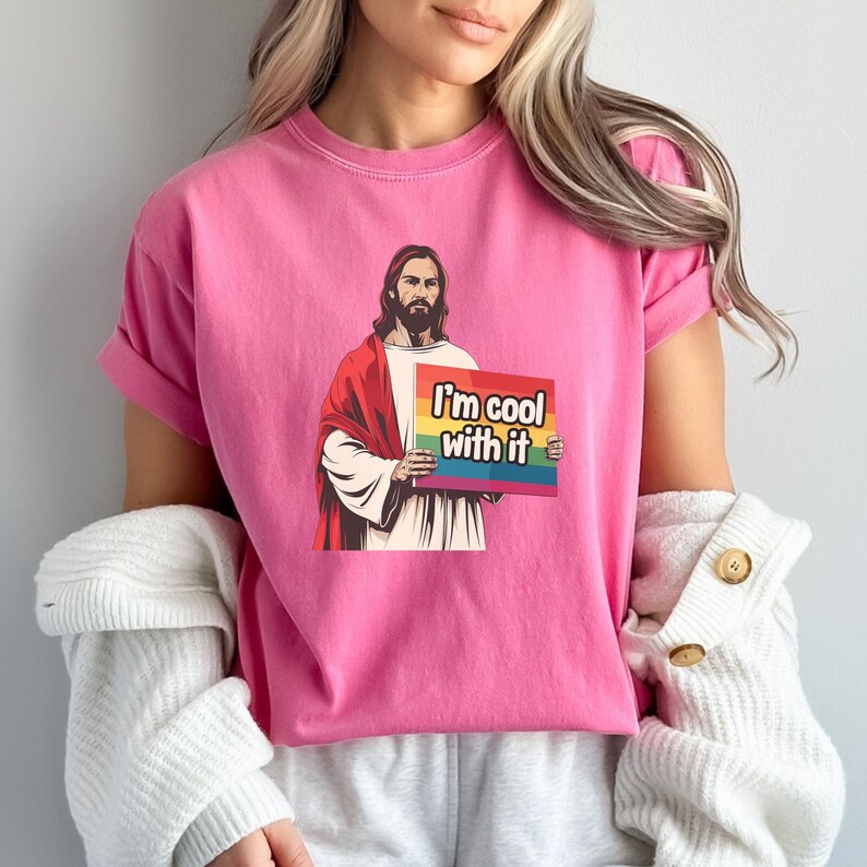 May include: Pink t-shirt with a graphic of Jesus holding a rainbow flag that says "I'm cool with it".