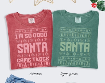 May include: Two crewneck t-shirts in crimson and light green. The crimson shirt features pink text reading I'M SO GOOD SANTA CAME TWICE with snowflake and tree patterns. The green shirt features light green text reading SANTA with similar patterns.
