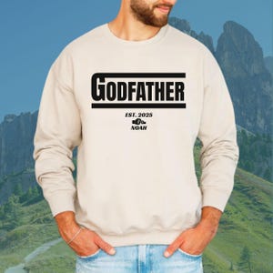 May include: A beige sweatshirt with black text that reads "GODFATHER EST. 2025 NOAH" with a graphic of two boxing gloves.
