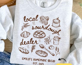Könnte beinhalten: Ein graues Sweatshirt mit einem braunen Grafikdesign aus Brot, Mehl und einem Löffel. Der Text auf der Grafik lautet "local sourdough dealer" und "Emily's Homemade Bread Est. 2024". Es gibt Platz für einen individuellen Namen.