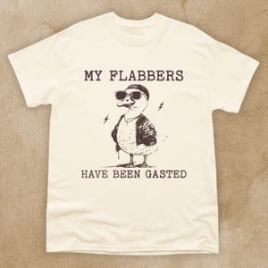Puede incluir: Una camiseta blanca con un gr&aacute;fico marr&oacute;n de un pato con gafas de sol y una gorra. El texto "My flabbers have been gasted" est&aacute; impreso en la camiseta.