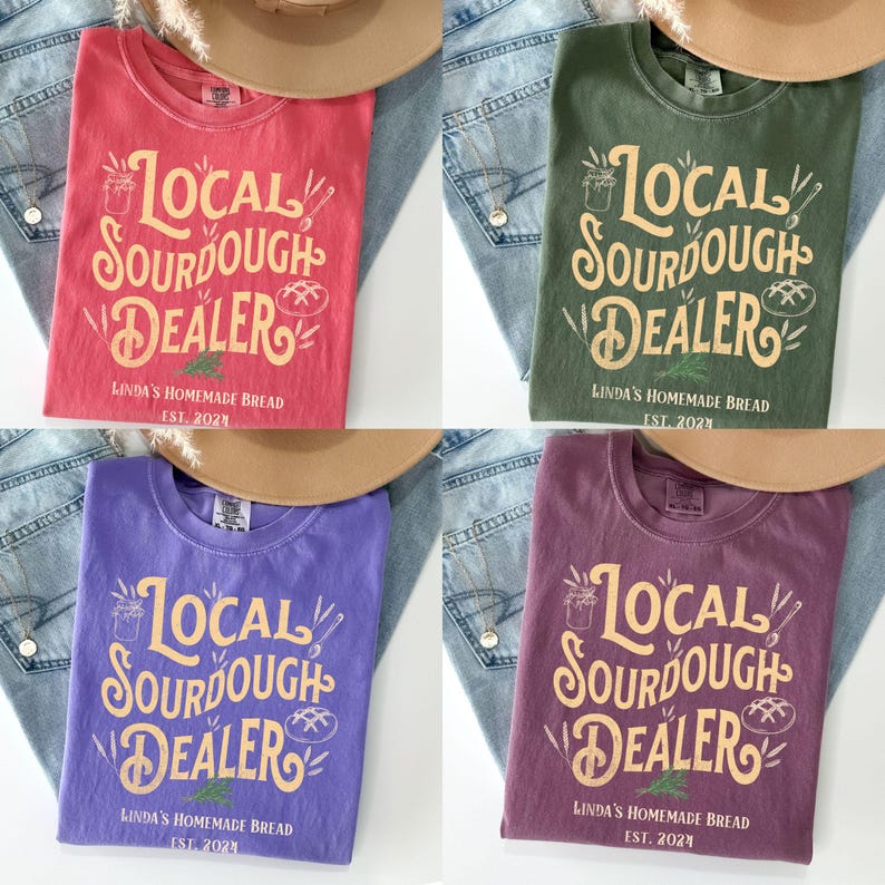 Peut inclure: Quatre t-shirts de couleurs diff&eacute;rentes avec le texte "Local Sourdough Dealer" dans une police de caract&egrave;res de style vintage. Le texte est en jaune avec un contour brun. Les chemises sont rouge, verte, violette et marron.
