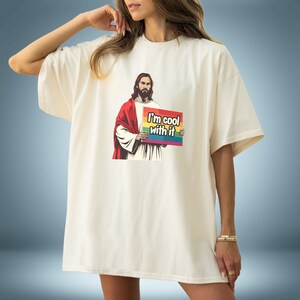 May include: A white t-shirt with a graphic of Jesus holding a sign that says "I'm cool with it". The sign has a rainbow stripe design.