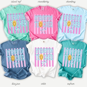 May include: Six short-sleeved t-shirts in various colors, including blue, pink, and white. Each shirt features the text "INTERVENTION TEACHER" in a playful font, with a smiling face and bow graphic. The shirts are a casual style.