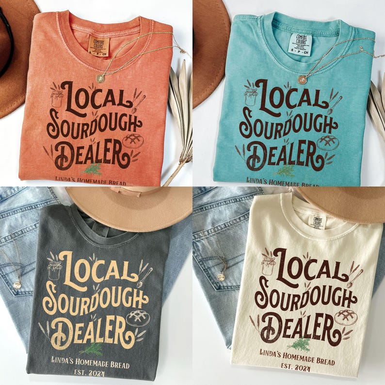 Peut inclure: Quatre t-shirts de couleurs diff&eacute;rentes avec le texte "Local Sourdough Dealer" et "Linda's Homemade Bread" imprim&eacute; dessus. Les t-shirts sont pr&eacute;sent&eacute;s sur une surface en bois avec un jean et un chapeau.