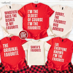 Könnte beinhalten: Eine Kollektion von fünf kurzärmeligen T-Shirts in Rot und Naturfarben. Die Shirts zeigen abgenutzten weißen oder roten Text, darunter Phrasen wie WHOEVER DOES THE DISHES IS MY FAVORITE, I'M THE OLDEST OF COURSE I'M THE FAVORITE, SORRY THE FAVORITE HAS ARRIVED, THE ORIGINAL FAVORITE, SANTA'S FAVORITE und LOL EVERYONE KNOWS I'M THE FAVORITE.