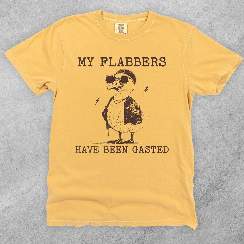 Puede incluir: Una camiseta amarilla con un pato de dibujos animados que lleva gafas de sol y una chaqueta de cuero. El texto "MY FLABBERS HAVE BEEN GASTED" est&aacute; impreso en la camiseta.