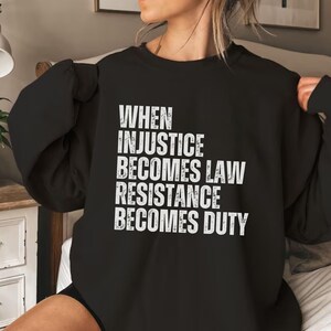 Pode incluir: Camisola de moletom preta com texto branco que diz "Quando a injustiça se torna lei, a resistência se torna dever."