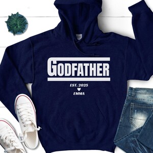 May include: Navy blue hooded sweatshirt with white text that reads "GODFATHER EST. 2025" with a white heart and the name "EMMA" underneath.