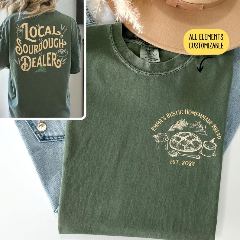 Pu&ograve; includere: Una maglietta verde con un design grafico bianco che dice "Emma's Rustic Homemade Bread" con un disegno di una pagnotta di pane, un barattolo, un cucchiaio e un sacchetto di farina. Il testo "Est. 2021" &egrave; sotto il grafico. Il testo "Tutti gli elementi personalizzabili" &egrave; nell'angolo in alto a destra dell'immagine.