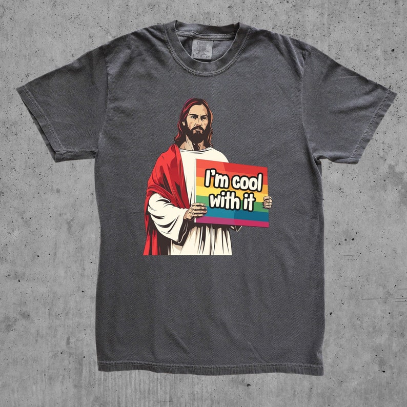 May include: A dark gray t-shirt with a graphic of Jesus holding a sign that says "I'm cool with it". The sign has a rainbow stripe across the top.