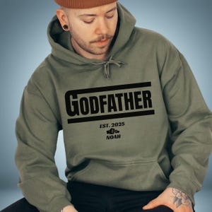 May include: A green hooded sweatshirt with the text "GODFATHER EST. 2025 NOAH" printed on the front.