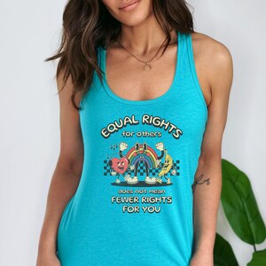 May include: Turquoise tank top with the text "EQUAL RIGHTS for others does not mean FEWER RIGHTS FOR YOU." The graphic features a heart, rainbow, and banana with arms and legs. The design has a retro, cartoon style.