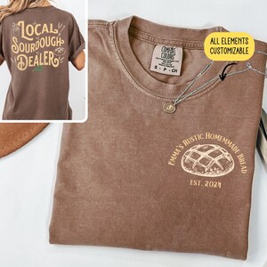 Pu&ograve; includere: Una maglietta marrone con una grafica di una pagnotta di pane e il testo "Emma's Rustic Homemade Bread Est. 2024". Il testo "Tutti gli elementi sono personalizzabili" &egrave; anche visibile nell'immagine.