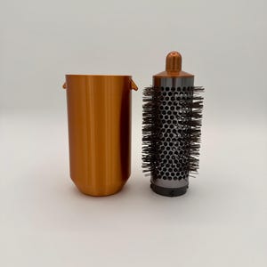 May include: A copper-colored cylindrical container and a round hair styling brush with black bristles. The brush has a perforated metal barrel and a copper-colored handle. The container is approximately 6 inches tall.