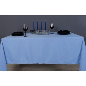 May include: A light blue tablecloth with a set of black plates and glasses on top. There are five blue candles in a silver holder in the center of the table.