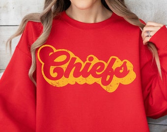 Puede incluir: Sudadera roja con un gráfico retro de "Chiefs" en amarillo y naranja.