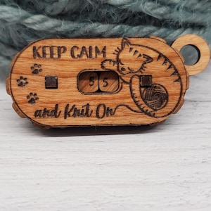 May include: Wooden knitting row counter with the text "Keep Calm and Knit On" and a cat design. The counter displays the number 55. Features paw prints and a small loop for attaching to a keychain.