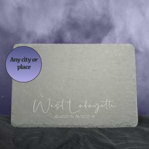 May include: A rectangular gray slate board with the text "West Lafayette" and coordinates. A purple circle with the text "Any city or place" is in the upper left corner. The background is a smoky purple.