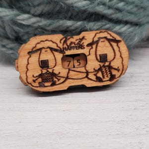 May include: Wooden knitting row counter with two sheep illustrations and the text "Knit Happens". The counter displays the number 75. The item is made of light brown wood and is designed for knitters.