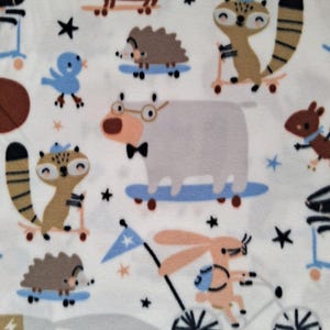 May include: White fleece fabric with a repeating pattern of cartoon animals, including a dachshund, raccoon, hedgehog, and bunny, riding skateboards, scooters, and a bicycle. The design also features stars and a blue bird.