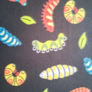 May include: Dark gray fabric with a repeating pattern of colorful caterpillars and green leaves. The caterpillars are in various colors, including red, yellow, blue, and green, with detailed designs. The leaves are a bright green.