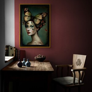 May include: A framed print of a woman with a butterfly on her head. The woman's face is covered in butterflies and she has a dark background. The frame is gold and the print is on a wall in a room with a wooden table and chairs.