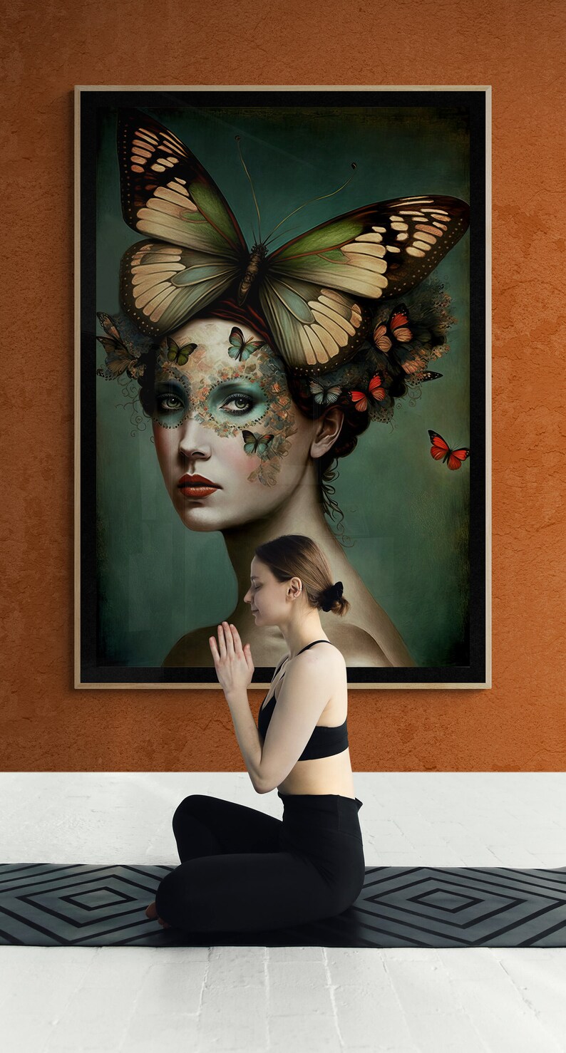 May include: A woman sits in a yoga pose on a black yoga mat in front of a framed painting of a woman with butterflies on her face. The painting has a dark green background.