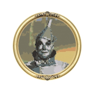 May include: A framed cross-stitch of the Tin Man from The Wizard of Oz. The Tin Man is depicted in a silver and grey colour scheme with a red and green hat. The frame is gold with ornate detailing.