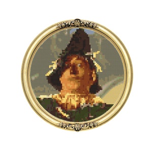 May include: A framed cross-stitch portrait of the Scarecrow from the Wizard of Oz. The Scarecrow is wearing a brown hat and a green shirt. The background is a green and brown landscape.