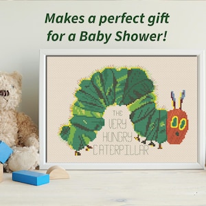 May include: A framed cross-stitch of The Very Hungry Caterpillar, a classic children's book character. The caterpillar is green and has a red head with two yellow eyes. The text "The Very Hungry Caterpillar" is stitched in yellow and black.