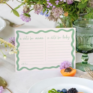A note card with a green border and a blank space for writing is placed on a table with a vase of flowers, a glass of water, and a plate of food.