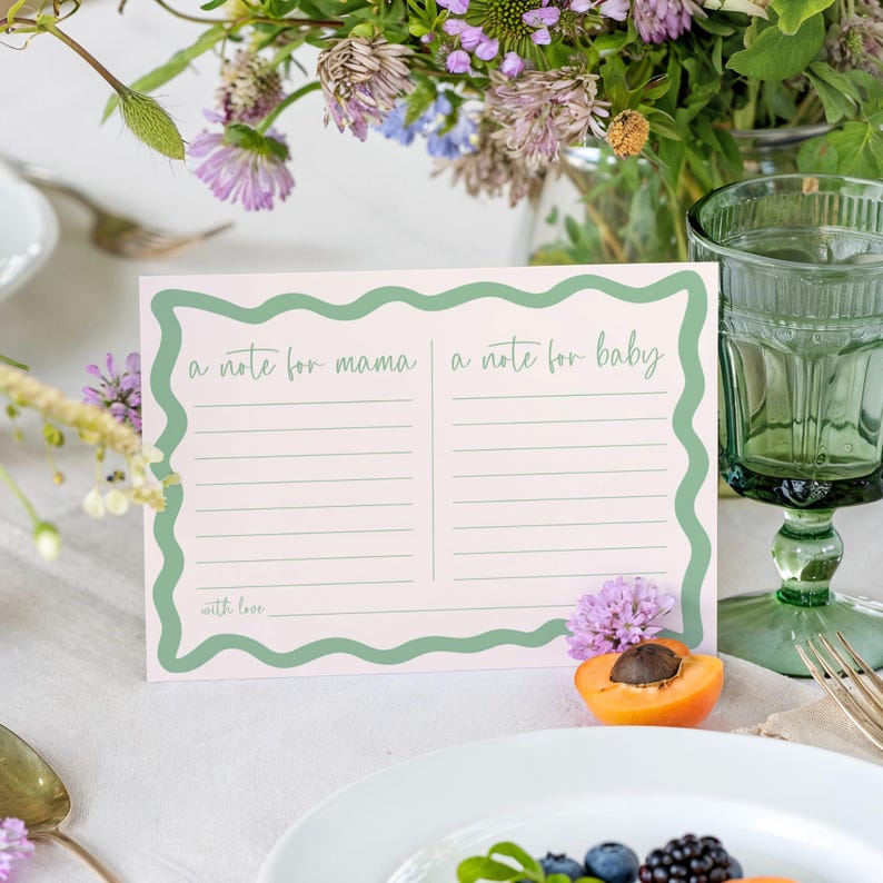 A note card with a green border and a blank space for writing is placed on a table with a vase of flowers, a glass of water, and a plate of food.
