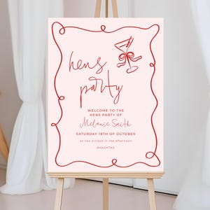 a pink sign with red cursive text and a graphic of a wine glass, welcoming guests to a hens party.