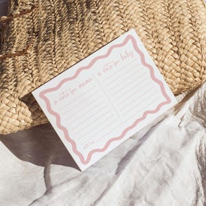A note card with a pink border and blank lines is placed on a woven straw mat.