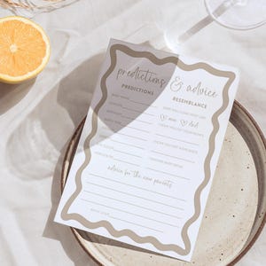 Boho wave baby shower prediction and advice for parents card gender neutral baby shower game design editable template laid on a simple plate with lemon slice and glass shadow over neutral linen background styled for modern shower decor printable card activity inviting guests to predict baby details and offer advice for the new parents