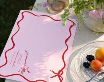 Könnte beinhalten: Eine rechteckige hellrosa Karte mit einem wellenförmigen roten Rand und einer roten Schleife unten rechts. Der Text lautet: jasmine, WELCOME TO THE BRIDAL SHOWER OF Melanie Smith, SATURDAY 18TH OF OCTOBER, mit einem Martini-Glas-Symbol.