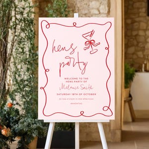 a pink sign with red text and a red ribbon design, welcoming guests to a party.