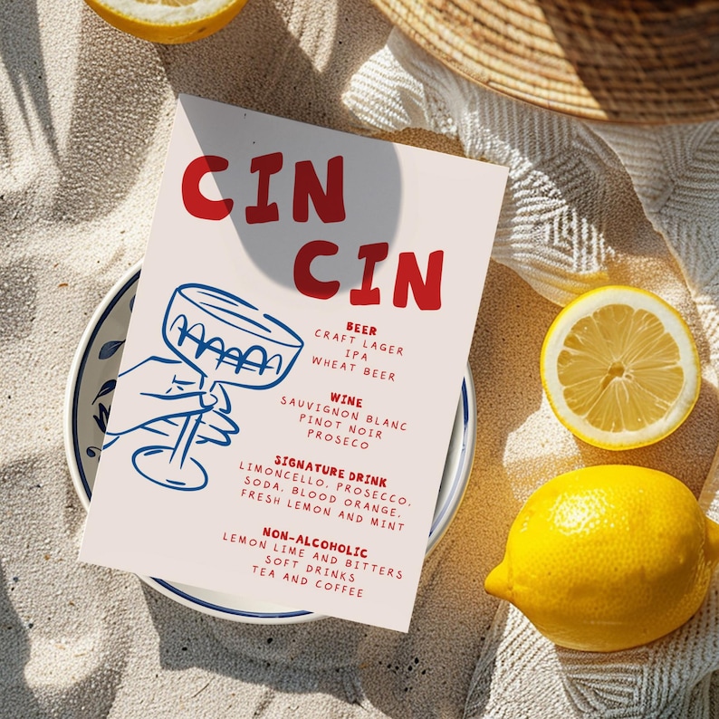 May include: A menu card with the words "CIN CIN" in red, featuring a cocktail glass illustration. The menu lists beer, wine, signature drinks, and non-alcoholic beverages. Yellow lemons and a plate with a blue floral design are also visible.