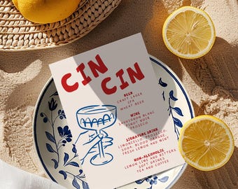 May include: A menu card with the text CIN CIN, featuring a blue line drawing of a hand holding a glass. The menu lists beer, wine, signature drinks, and non-alcoholic options. It rests on a white plate with blue floral patterns.