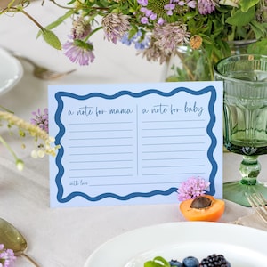 May include: A light blue rectangular card with a dark blue wavy border. The card features two columns with horizontal lines labeled "a note for mama" and "a note for baby," with the text "with love" at the bottom left corner.