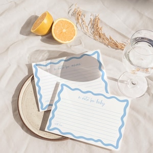 Puede incluir: Dos tarjetas de papelería rectangulares blancas con bordes ondulados de color azul claro. Una tarjeta presenta el texto "a note for mama" y la otra "a note for baby", ambas con líneas horizontales y la frase "with love" al pie.