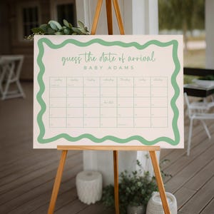 a guessing game board for the date of arrival of a baby named Adams. The board is set up on a wooden easel, with a potted plant and a chair visible in the background.