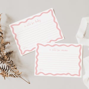 two blank note cards with a pink border, placed on a light-colored surface alongside some dried leaves.